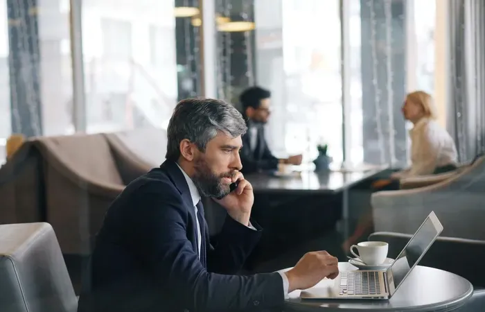 Business owner in a cafe on a phone call using a laptop, showing why locals trust Town Biz Index to find services